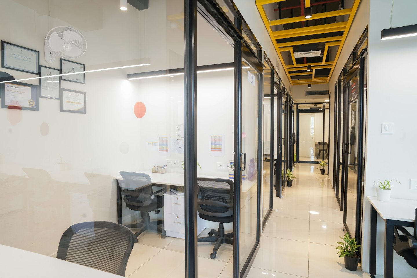 Pasillo de oficina moderno con espacios de trabajo privados y techos de rejilla amarillos.